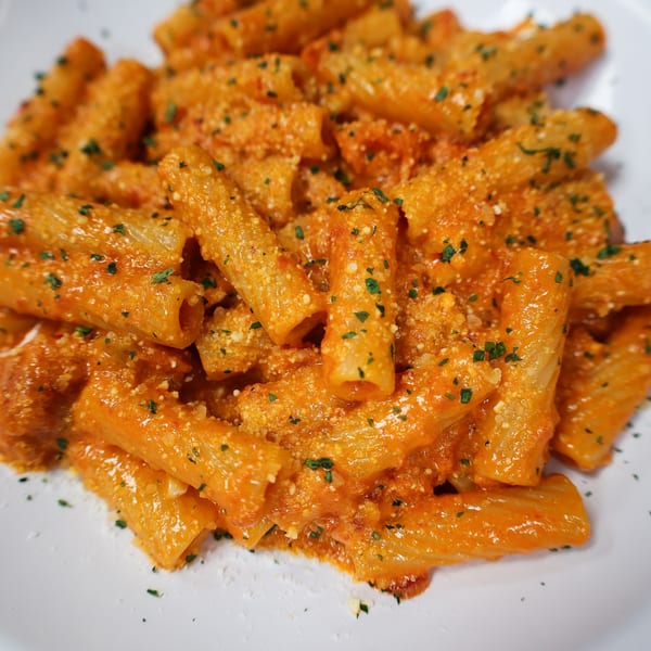 Close-up of rigatoni pasta in a creamy orange sauce, topped with grated cheese and parsley.