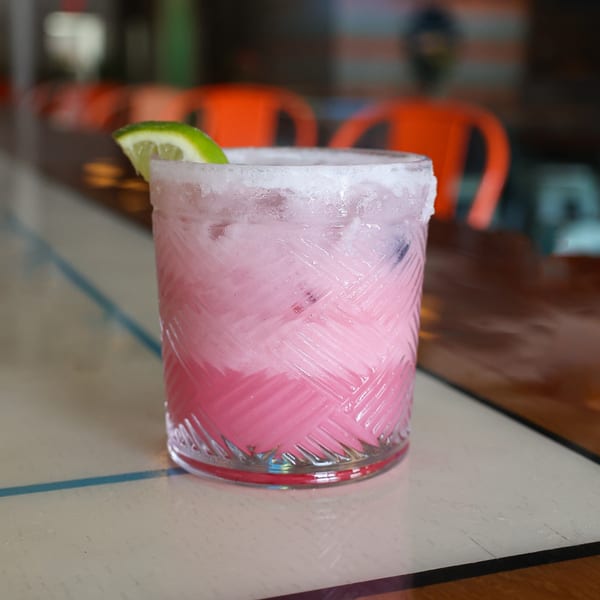 Pink cocktail with a salted rim and lime wedge on a bar top at Spycoast Kitchen & Cocktails.