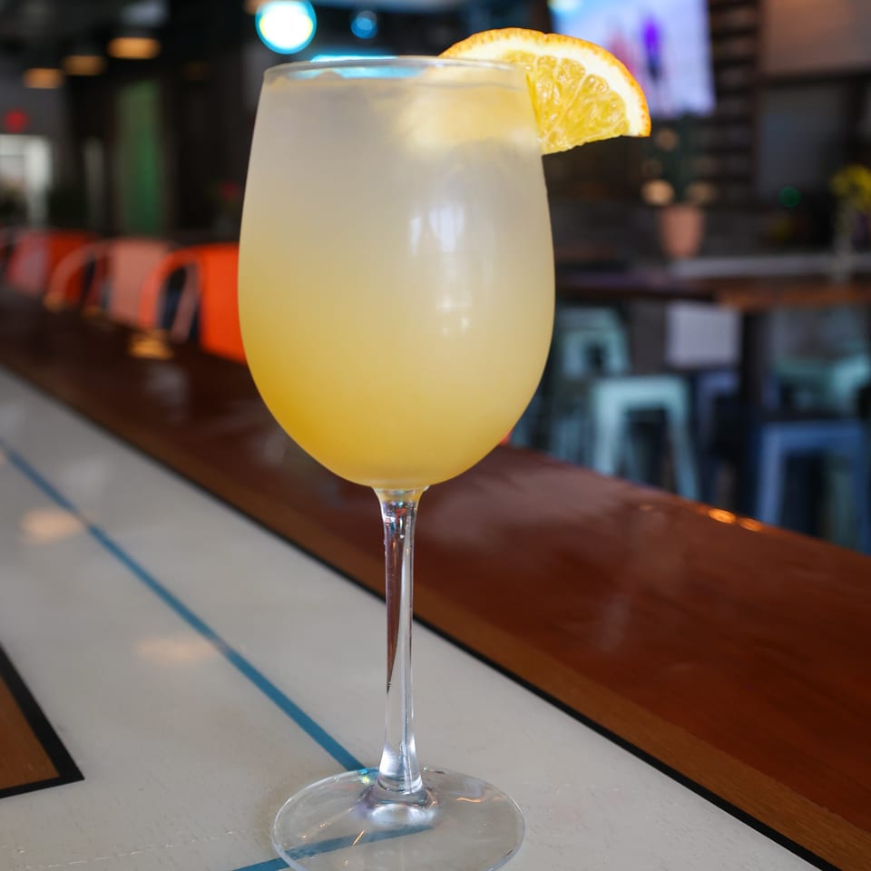 A Spycoast Kitchen & Cocktails mimosa with an orange slice garnish sits on a bar.
