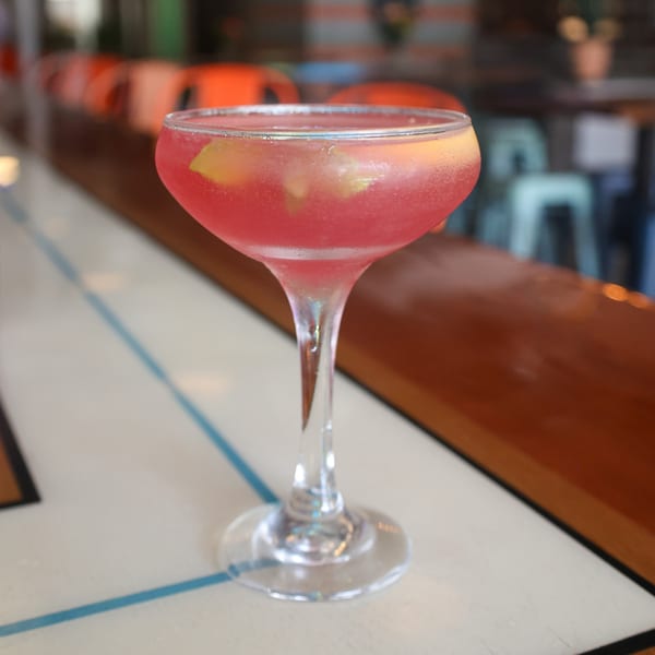 A vibrant pink cocktail with lemon slices and ice sits on a bar at Spycoast Kitchen & Cocktails.