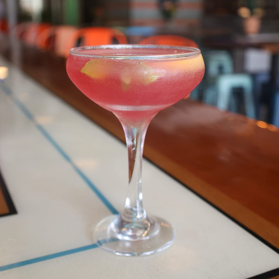 A vibrant pink cocktail with lemon slices and ice sits on a bar at Spycoast Kitchen & Cocktails.