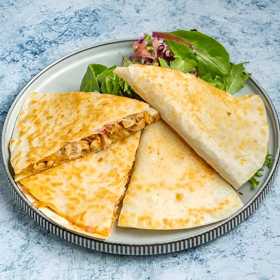 Golden-brown quesadillas, one cut open to reveal chicken and cheese filling, served with a side salad.