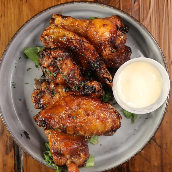Spycoast Kitchen & Cocktails' glazed chicken wings with a side of dipping sauce on a gray plate.